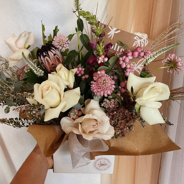 Large vase arrangement with protea, roses, and seasonal flowers in pastels, pinks and burgundy pallet