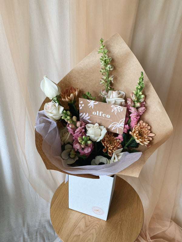 Bouquet of fresh, seasonal Flowers in pastel pink & peach colours, wrapped in kraft paper and displayed in a delivery box