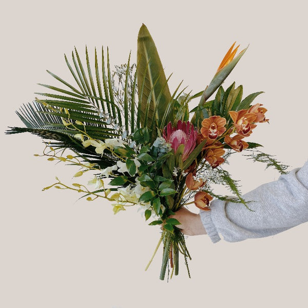 A tropical flower bouquet with palm leaves, orchids, protea and birds of paradise flower and cymbidium orchids