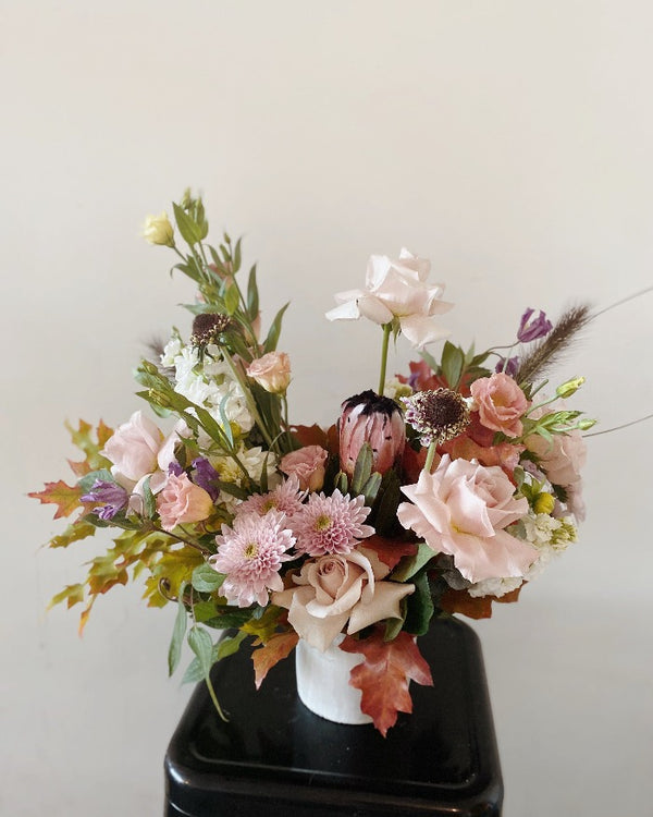 Designers choice flower arrangement with vase with seasonal greenery and pastel roses.