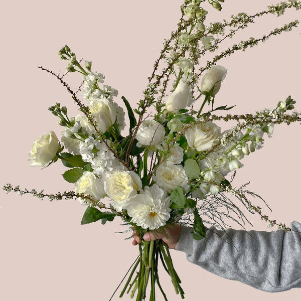 A botanical handtied flower arrangement with white roses, white mums and white delphinium
