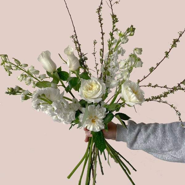 A botanical handtied flower arrangement with white roses, white mums and white delphinium