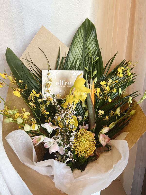 A tropical flower and foliage birthday bouquet with yellow orchids, pink dendrobium, pincushion and birds of paradise
