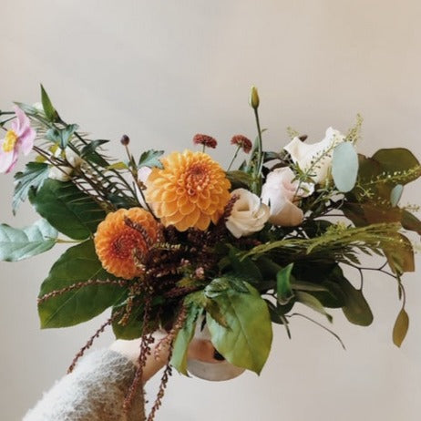 Funeral centerpiece arrangement with white roses and orange dahlias, salal and ferns