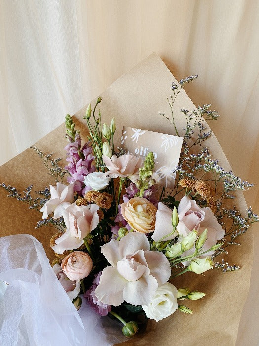 Seasonal bouquet with pastel roses, snap dragons, ranunculus and filler wrapped in kraft paper