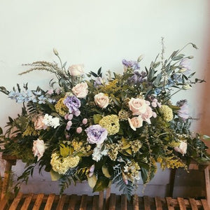 casket spray in botanical style with purples and greens and white. roses and westcoast greenery