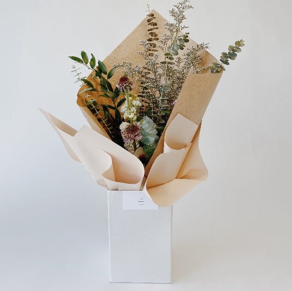 Wild textured bouquet with baby blue eucalpytus, limonium filler, anemone and scabiosa in an upright delivery box wrapped in kraft paper
