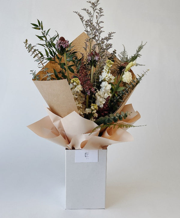 Wild textured bouquet with baby blue eucalpytus, limonium filler, anemone and scabiosa in an upright delivery box wrapped in kraft paper