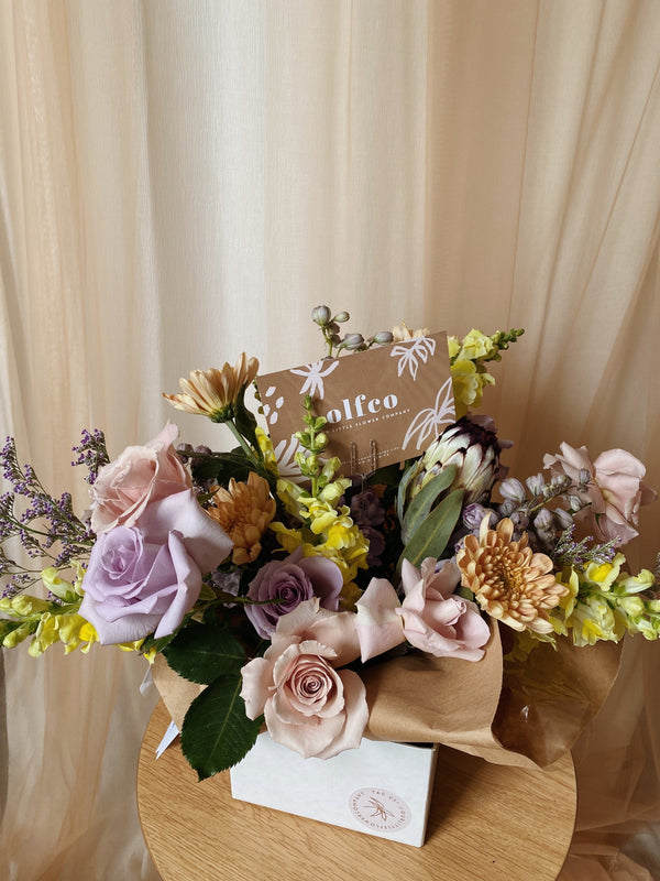 low arrangement in white box with pinks, purples and yellows