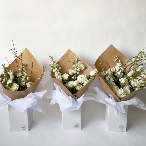 Three sizes of botanical handtied flower arrangement with white roses, white mums and white delphinium displayed in upright delivery box